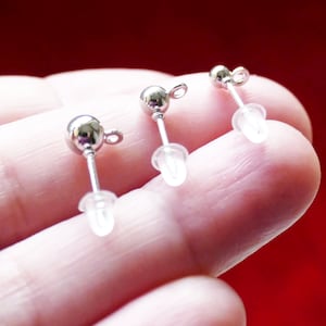 May include: Three silver earring posts with clear plastic stoppers. The posts are round and have a small loop at the top.