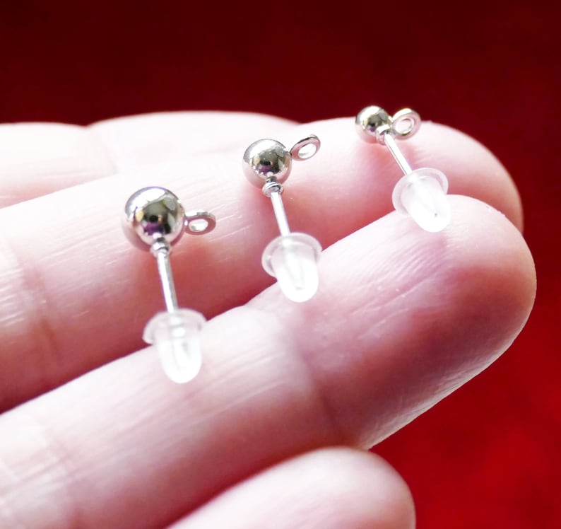 May include: Three silver earring posts with clear plastic stoppers. The posts are round and have a small loop at the top.