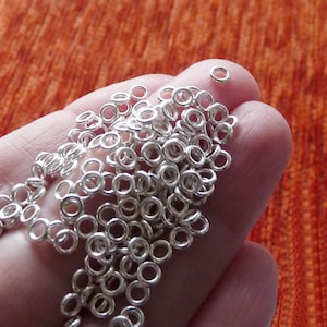 Peut inclure: Une main tient une grande pile d'anneaux de saut en argent, un type de trouvaille de bijoux. Les anneaux sont petits et ronds, et ils sont tous de la même taille.