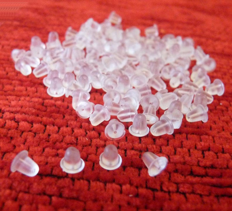 Puede incluir: Un mont&oacute;n grande de respaldos de pendientes de pl&aacute;stico transparente sobre una superficie roja texturizada.