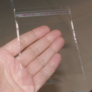 Może przedstawiać: Przezroczysty plastikowy woreczek z taśmą uszczelniającą. Na taśmie nadrukowany jest tekst "CHENG JIA * SEALING TAPE REMOVE LINER".