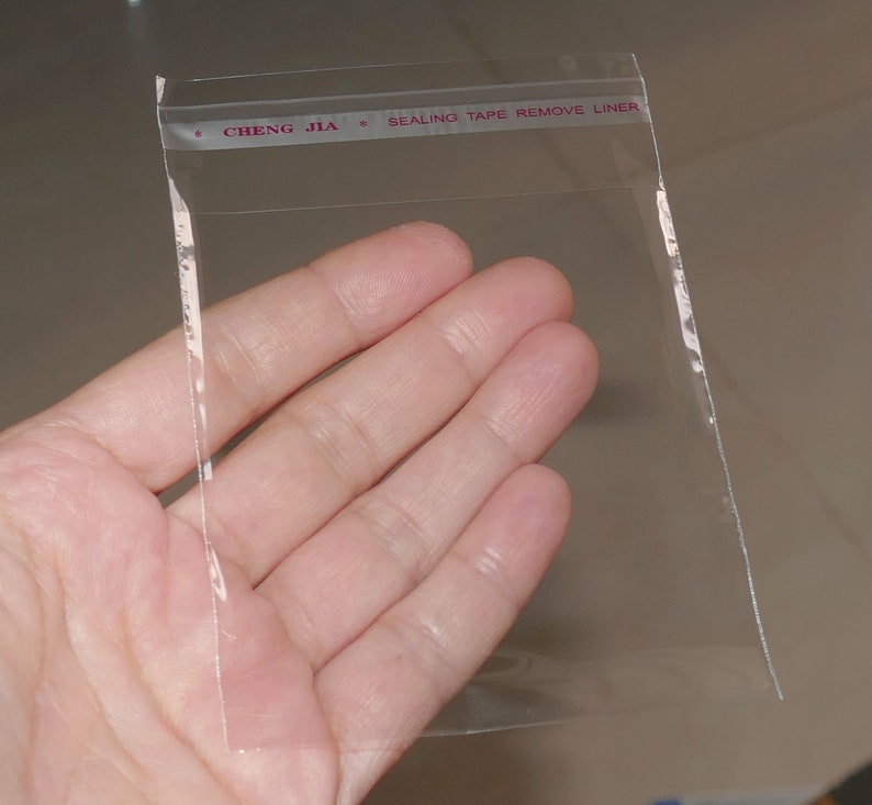 Może przedstawiać: Przezroczysty plastikowy woreczek z taśmą uszczelniającą. Na taśmie nadrukowany jest tekst "CHENG JIA * SEALING TAPE REMOVE LINER".