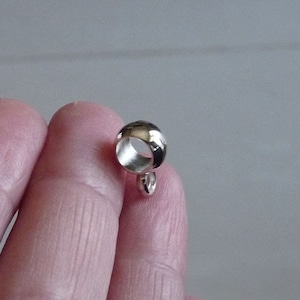 May include: Silver-toned metal ring with a small loop on the bottom. The ring is smooth and shiny.