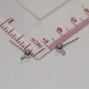 May include: Two silver earring findings with a small ball at the end and a loop for attaching jewelry. The findings are measured against a ruler.