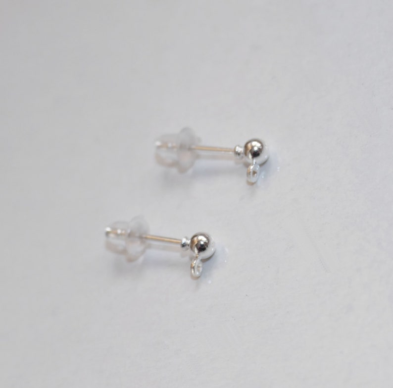 Puede incluir: Dos hallazgos de pendientes de plata con una peque&ntilde;a bola en la parte superior y un bucle en la parte inferior. Los hallazgos est&aacute;n unidos a respaldos de pendientes de pl&aacute;stico transparente.