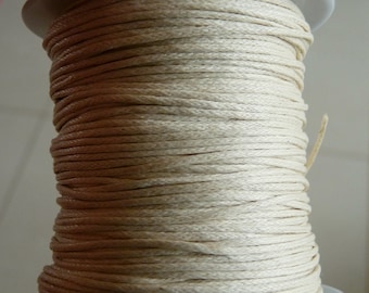 May include: A spool of natural-colored cotton cord wound around a white plastic bobbin. The cord is smooth and tightly wound.
