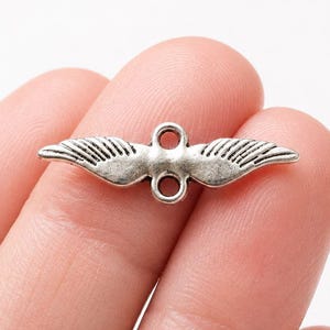 May include: A silver-coloured metal charm shaped like a bird with spread wings. It features two loops for attachment and detailed feather etching. The wingspan is approximately 3.8 cm.