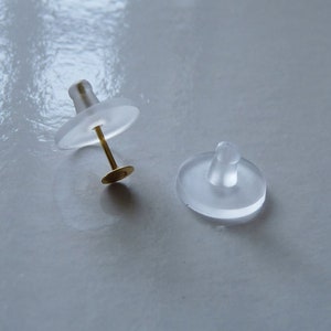 May include: Two clear plastic earring backs, one with a gold post and a small round disc at the end.