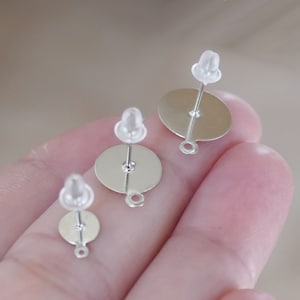 Op de afbeelding: Drie zilveren oorbelpennen met ronde achterkanten, de grootste is ongeveer 3,8 cm in diameter, de middelste is ongeveer 2,5 cm in diameter en de kleinste is ongeveer 1,3 cm in diameter.