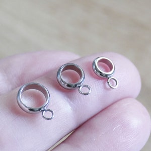 Peut inclure: Trois embouts de perles en m&eacute;tal argent&eacute; en forme d'anneau avec une petite boucle sur le c&ocirc;t&eacute;. Les embouts de perles sont sur un doigt.