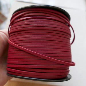May include: A spool of burgundy leather cord, wound tightly in a coil. The cord is smooth and has a slight sheen.