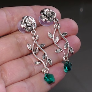 May include: Silver earrings with a floral design and green gemstone drops. The earrings feature a delicate vine design with leaves and a small flower at the top.