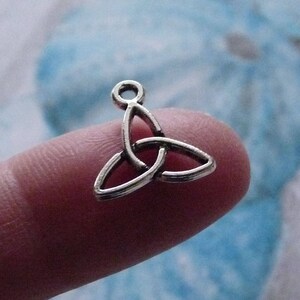 Könnte beinhalten: Silberner keltischer Knoten-Anhänger in Form eines Dreiecks. Der Anhänger befindet sich auf einem Finger.