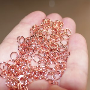 May include: A large pile of small, rose gold jump rings. The rings are all the same size and are arranged in a random pattern.