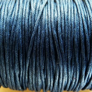 May include: A close-up of a spool of dark blue waxed cotton cord. The cord is tightly wound and has a smooth, polished finish.