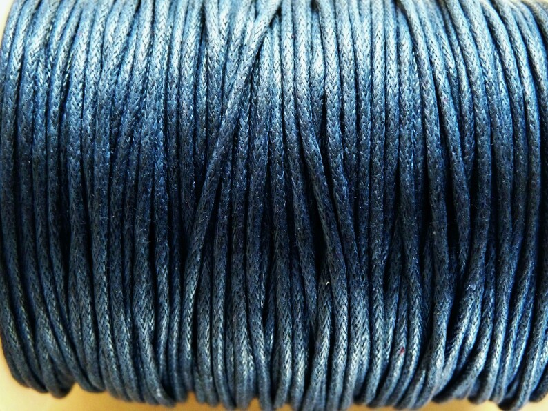 May include: A close-up of a spool of dark blue waxed cotton cord. The cord is tightly wound and has a smooth, polished finish.