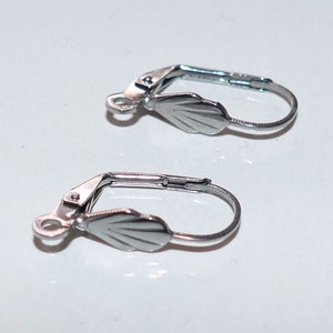 May include: Two silver-toned earring clips with a scalloped design. The clips are made of metal and have a spring-loaded mechanism.