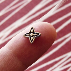 May include: A silver-toned metal charm in the shape of a four-pointed star with a small circle in the center.