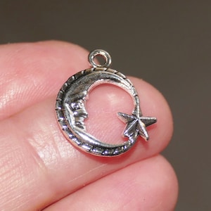 May include: Silver charm featuring a crescent moon with a star inside. The moon has a face and the star has five points.