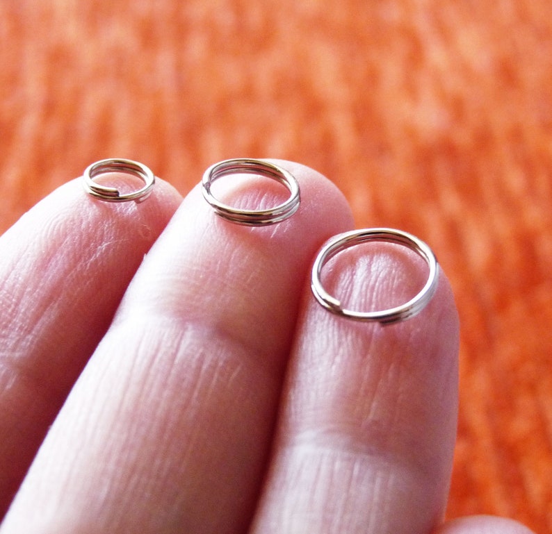 May include: Three silver jump rings of different sizes, held on fingers.