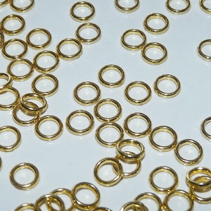 Puede incluir: Una gran cantidad de anillos de salto dorados, un tipo de hallazgo de joyer&iacute;a, esparcidos sobre una superficie blanca.