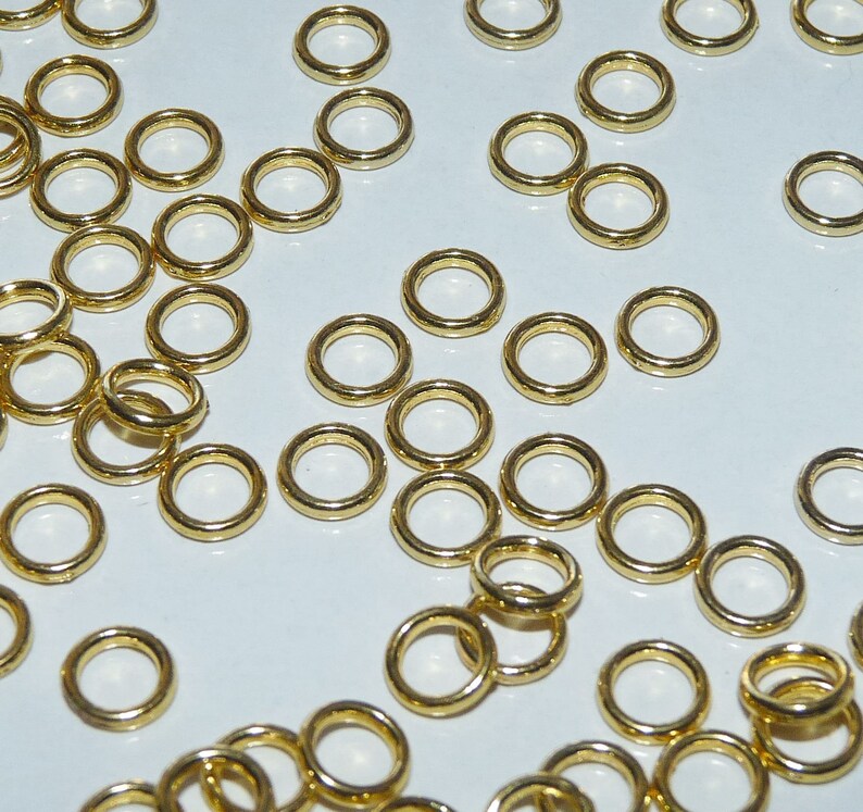 Puede incluir: Una gran cantidad de anillos de salto dorados, un tipo de hallazgo de joyer&iacute;a, esparcidos sobre una superficie blanca.