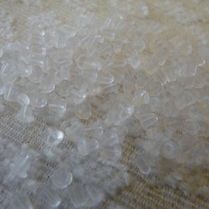 Puede incluir: Una gran cantidad de respaldos de pendientes de pl&aacute;stico transparente esparcidos sobre una superficie de tela blanca.