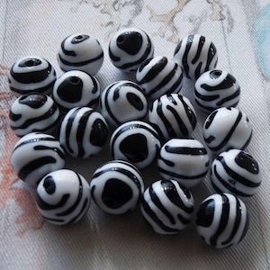 Pode incluir: Uma coleção de contas redondas de plástico com estampa de zebra em preto e branco. As contas têm um acabamento brilhante.