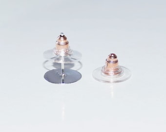 May include: Two clear plastic earring backs with a rose gold colored metal post and a round top. The earring backs are designed to be used with stud earrings.