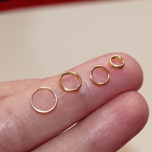 Op de afbeelding: Vijf gouden springringen in verschillende maten, getoond op een vinger.