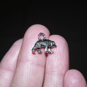 May include: Silver charm in the shape of a bear walking. The charm is small and detailed.