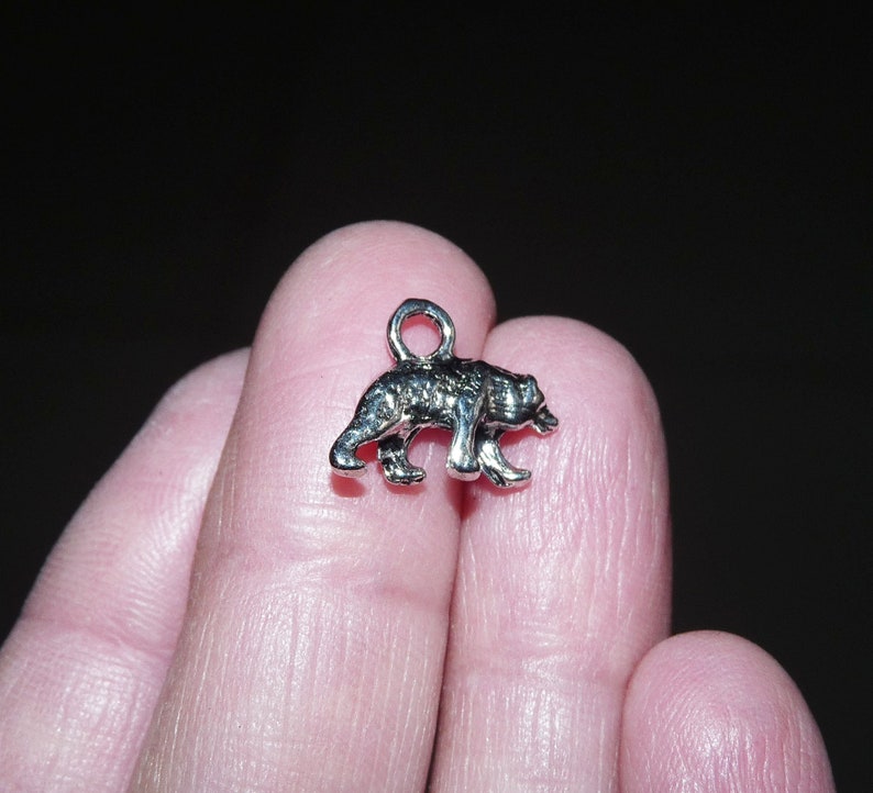 May include: Silver charm in the shape of a bear walking. The charm is small and detailed.