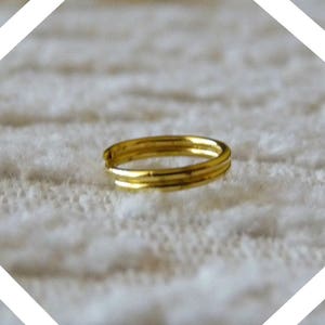 Può includere: Un anello dorato con un design a doppia fascia. L'anello è su una superficie bianca.