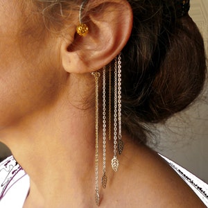 Puede incluir: Un pendiente de oreja dorado y plateado con múltiples cadenas y colgantes en forma de hoja.