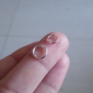 May include: Two silver jump rings, one larger than the other, are shown on a finger.