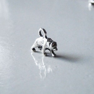 May include: Silver charm in the shape of a bear standing on all fours. The bear is facing to the right and has a loop at the top for attaching to a necklace or bracelet.