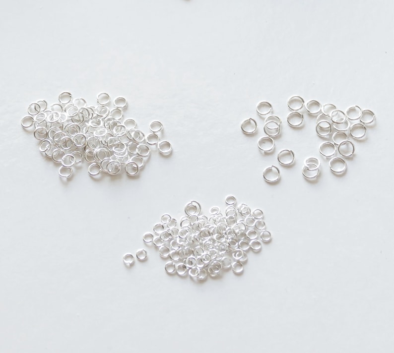 May include: A pile of silver jump rings, a popular jewellery making supply, on a white background.