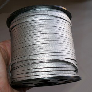 May include: A spool of silver leather cord, wound tightly on a black plastic spool.