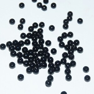Peut inclure: Un grand tas de perles rondes noires, avec quelques-unes éparpillées sur une surface blanche.