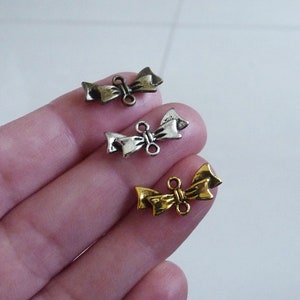 Puede incluir: Tres abalorios de lazo de metal en dorado, plateado y bronce. Cada abalorio tiene un lazo doble para sujetarlo a joyas u otras manualidades.