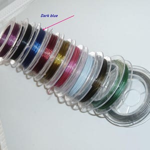 Op de afbeelding: Een stapel spoelen met gekleurde draad, waaronder zilver, goud, rood, roze, blauw, groen en zwart. De spoelen zijn spiraalsgewijs gerangschikt, met de donkerblauwe spoel bovenaan. De tekst "Dark blue" is in blauw boven de spoel geschreven.