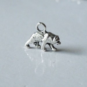 May include: Silver charm of a walking bear. The bear is facing right and has a loop at the top for attaching to a necklace or bracelet.