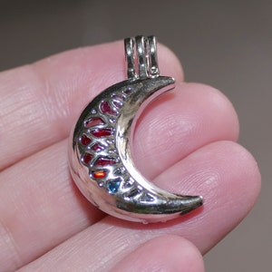 Può includere: Un ciondolo a forma di mezzaluna d'argento con un design in smalto rosso, arancione e blu. Il ciondolo ha un anello nella parte superiore per attaccarlo a una collana o un braccialetto.