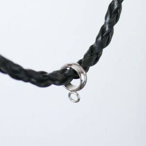 Peut inclure: Un cordon en cuir tress&eacute; noir avec une bague argent&eacute;e et une petite boucle attach&eacute;e.