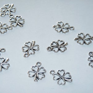 May include: A collection of silver-toned metal charms shaped like four-leaf clovers. Each charm has a loop at the top for attaching to jewelry or other crafts.