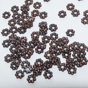 May include: A large quantity of small, bronze-colored metal flower-shaped jump rings. The rings are about 1/2 inch in diameter and have a hole in the center.