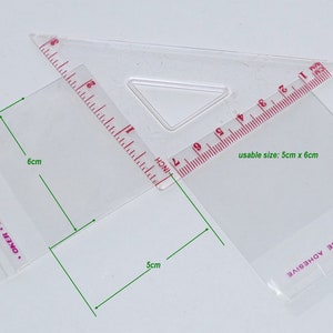 Puede incluir: Una bolsa de pl&aacute;stico transparente con una regla roja y blanca adjunta. La bolsa tiene un tama&ntilde;o &uacute;til de 5 cm por 6 cm. La bolsa tiene el texto "OKER BRAND SEALING" y "OVE LINER TO EXPOSE ADHESIVE" impreso en ella.