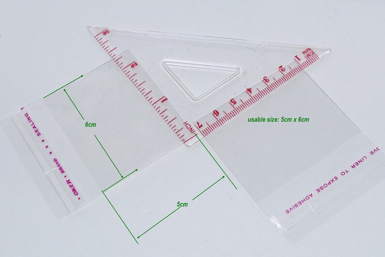 Puede incluir: Una bolsa de pl&aacute;stico transparente con una regla roja y blanca adjunta. La bolsa tiene un tama&ntilde;o &uacute;til de 5 cm por 6 cm. La bolsa tiene el texto "OKER BRAND SEALING" y "OVE LINER TO EXPOSE ADHESIVE" impreso en ella.