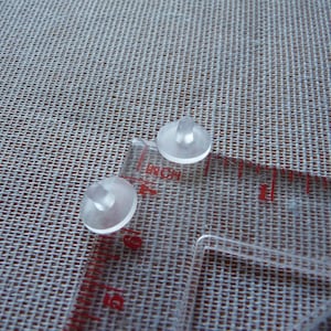 May include: Two clear plastic sewing tools with a small knob on top. The tools are on a white fabric surface with a clear ruler.