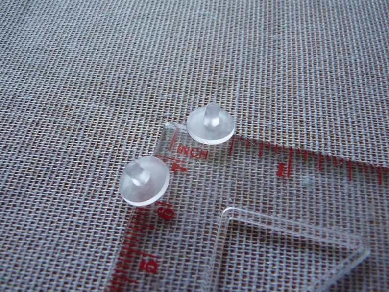 May include: Two clear plastic sewing tools with a small knob on top. The tools are on a white fabric surface with a clear ruler.